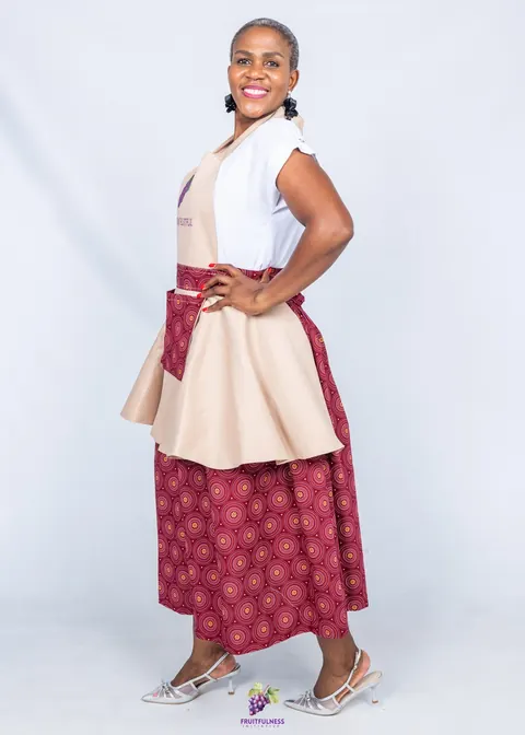 Side view of a woman smiling in a beige apron with a maroon-print pocket and skirt